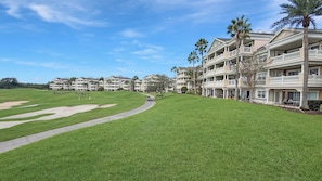 Ein Golfplatz mit Weg, ein Gebäude mit mehreren Balkonen und Palmen.
