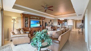 Ein großzügiges Wohnzimmer mit Fernseher, Ledersofas, einem Couchtisch mit Pflanzen und einem Deckenventilator.