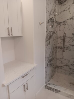 A bathroom with white cabinetry, a shower with marble walls, and a white countertop. - Delightful 1-bedroom cottage with AC in Dripping Springs (Dripping Springs)