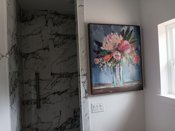 A bathroom with marble tiles, a shower, and a painting of flowers on the wall. - Delightful 1-bedroom cottage with AC in Dripping Springs (Dripping Springs)