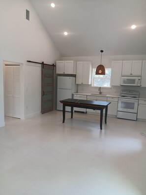 A kitchen with white cabinets, a refrigerator, a microwave, an oven, a dining table, and a hanging light fixture. - Delightful 1-bedroom cottage with AC in Dripping Springs (Dripping Springs)
