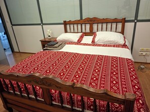 A bed with a patterned bedspread, a wooden headboard, and a nightstand with a lamp and books. - International Business (Pau)