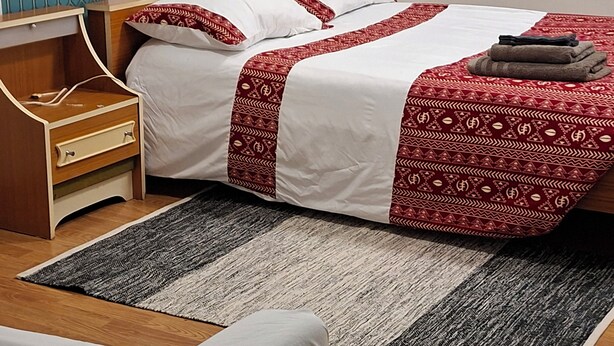 A neatly arranged bedroom with a bed, bedside table, and a rug. - International Business (Pau)