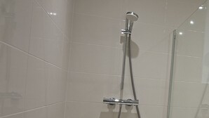 A shower with a handheld showerhead and a wall-mounted faucet in a tiled bathroom. - International Business (Pau)