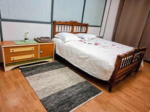 A bedroom with a wooden bed, a nightstand, a dresser, and a window with blinds. - International Business (Pau)