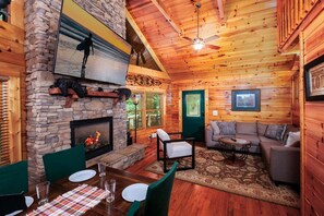 A cozy cabin interior with a stone fireplace, wooden walls, a ceiling fan, and a dining area. - Black Beary Lodge・Hot Tub・Pool Table・Community Pool・Arcade (Gatlinburg)