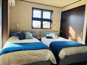 Habitación de hotel con dos camas, una ventana, un equipo de aire acondicionado y una puerta.