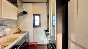 A narrow kitchen with a window, a red stool, and a towel hanging on the door. - Spacious villa in Hayama, 10 minutes walk to the beach, BBQ on the roof terrace! (Hayama)