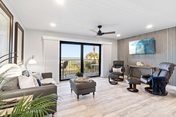 A modern living room with a sofa, armchairs, a coffee table, and a TV mounted on the wall. - Direct Oceanfront Condo | Balcony, Heated Pool + Putting Green 🍹🏝️ (Cocoa Beach)