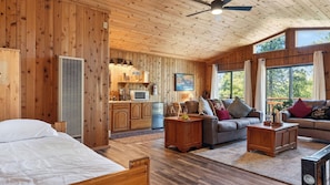 Ein Holzblockhaus-Interieur mit einem Bett, einer Couch, einem Essbereich und einer Küche.