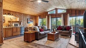 Ein Holzblockhaus mit Küche, zwei Sofas, einem Esstisch und großen Fenstern.