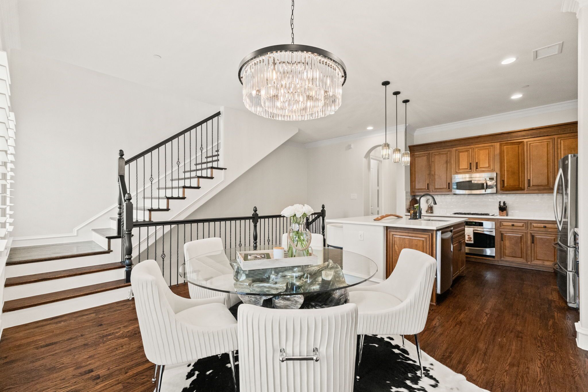 A modern kitchen with wooden cabinets, stainless steel appliances, and a glass dining table with white chairs.