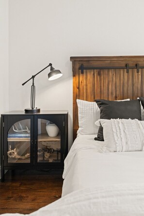 Un dormitorio con cama, mesita de noche con lámpara y cabecero de madera.