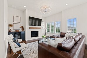 Una sala de estar moderna con chimenea, sofá de cuero y televisor grande.