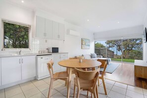 A modern kitchen with white cabinets, a wooden dining table, and a view of the outdoors. - Ultimate Ocean Views - Pet Friendly sleeps 20 (Jan Juc)