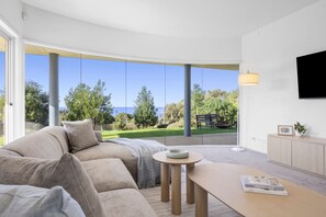 A modern living room with a sofa, a coffee table, and a TV mounted on the wall. - Ultimate Ocean Views - Pet Friendly sleeps 20 (Jan Juc)