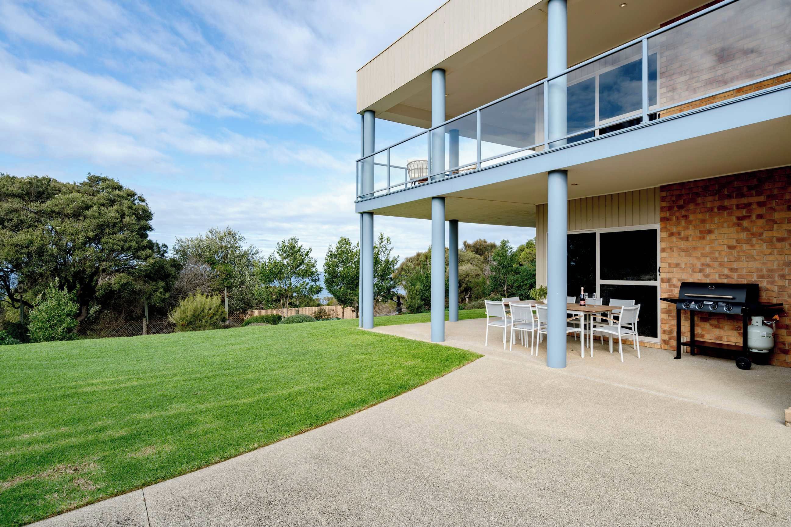 A modern two-story house with a balcony, a barbecue area, and a well-maintained lawn.