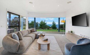 A modern living room with a large sofa, a coffee table, and a TV mounted on the wall. - Ultimate Ocean Views - Pet Friendly sleeps 20 (Jan Juc)