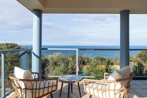 A balcony with wicker chairs and a glass table, overlooking a coastal landscape. - Ultimate Ocean Views - Pet Friendly sleeps 20 (Jan Juc)
