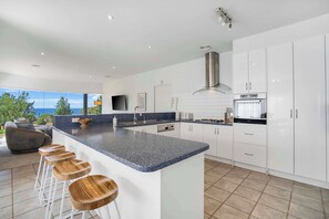 A modern kitchen with a large island, white cabinets, and a view of the outdoors. - Ultimate Ocean Views - Pet Friendly sleeps 20 (Jan Juc)