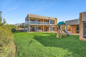 A two-story building with a balcony, a play area with a slide and swings, and a well-maintained lawn.