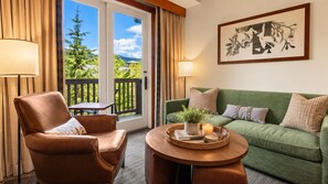 A room with a leather armchair, a green sofa, a small table with a candle, and a view of greenery through a glass door. - 2BR Spruce Peak condo with mountain views, fireplace, pool & hot tub (Stowe)