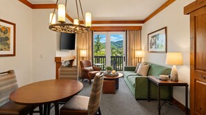 A hotel room with a dining table, a sofa, a chair, a lamp, and a television. - 2BR Spruce Peak condo with mountain views, fireplace, pool & hot tub (Stowe)