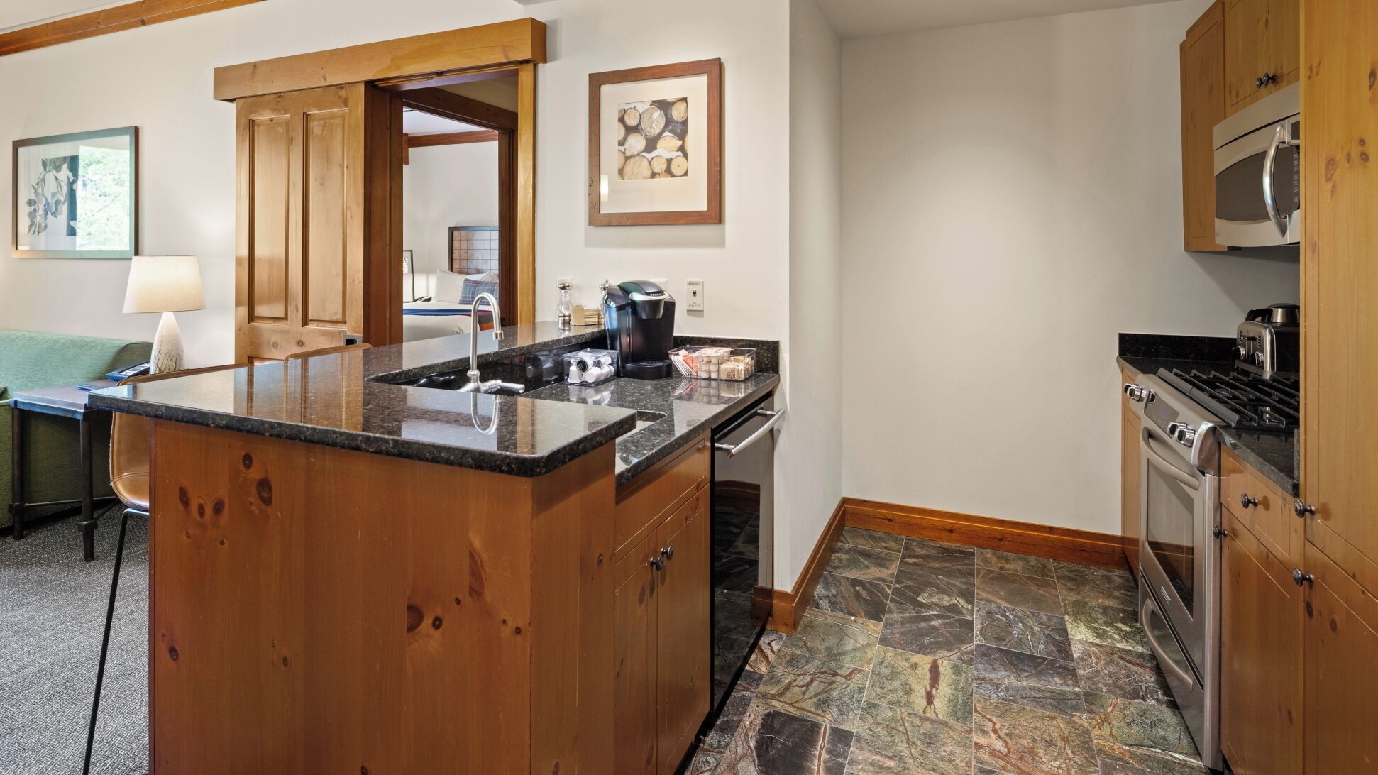 A kitchen with a granite countertop, wooden cabinets, a stainless steel oven, and a stone tile floor.