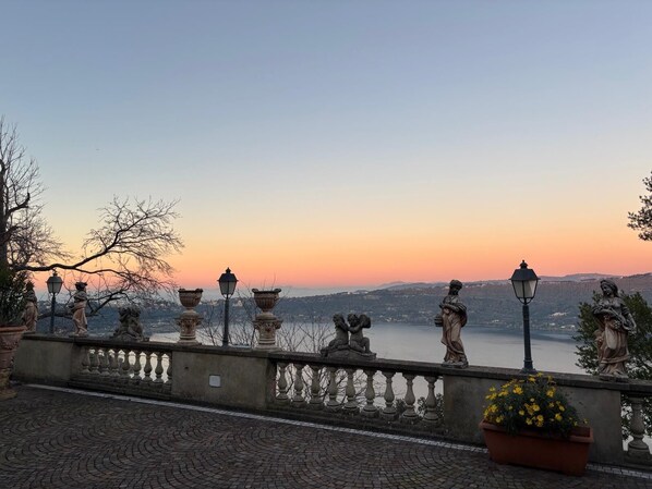 Una balaustra in pietra con statue e vista su uno specchio d'acqua al tramonto.