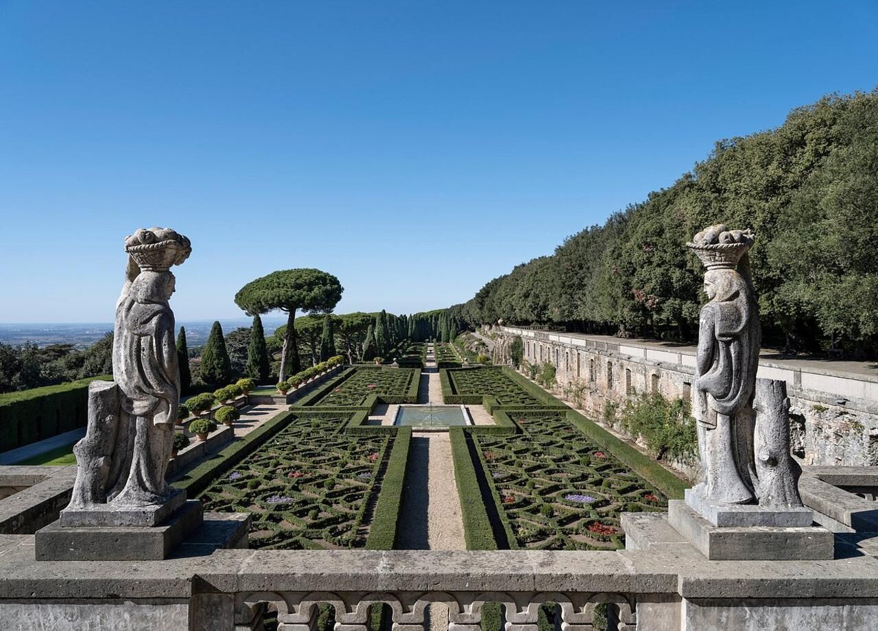 Un jardín formal con senderos simétricos, estatuas y una fuente central.