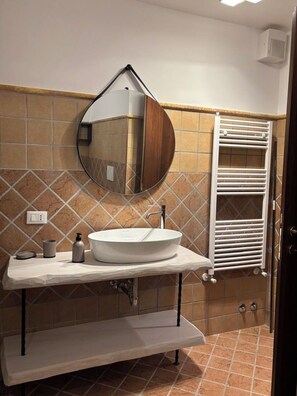 A bathroom with a round mirror, white sink, and a towel rack. - Vrbo Property (Castel Gandolfo)