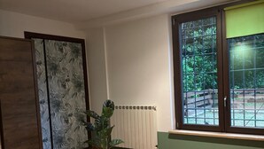 Een hotelkamer met een bed, een radiator, een raam met uitzicht op groen en een plant.
