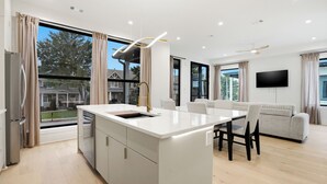 A modern kitchen with a central island, a dining area with a table and chairs, a sofa, and a flat-screen TV mounted on the wall. - New 3 Floor Luxury Custom Build with 3bed 3bath Private Patio and 1 Car Garage (Atlanta)