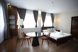 Hotellihuone, jossa on sänky, kaksi tuolia, pyöreä pöytä, lamppu ja vaatekaappi.