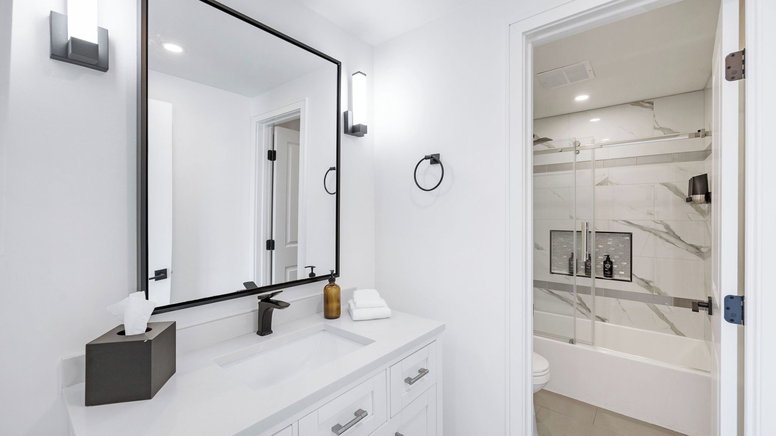 Une salle de bain moderne avec un grand miroir, un lavabo doté d’un distributeur de serviettes et une douche à parois de verre.