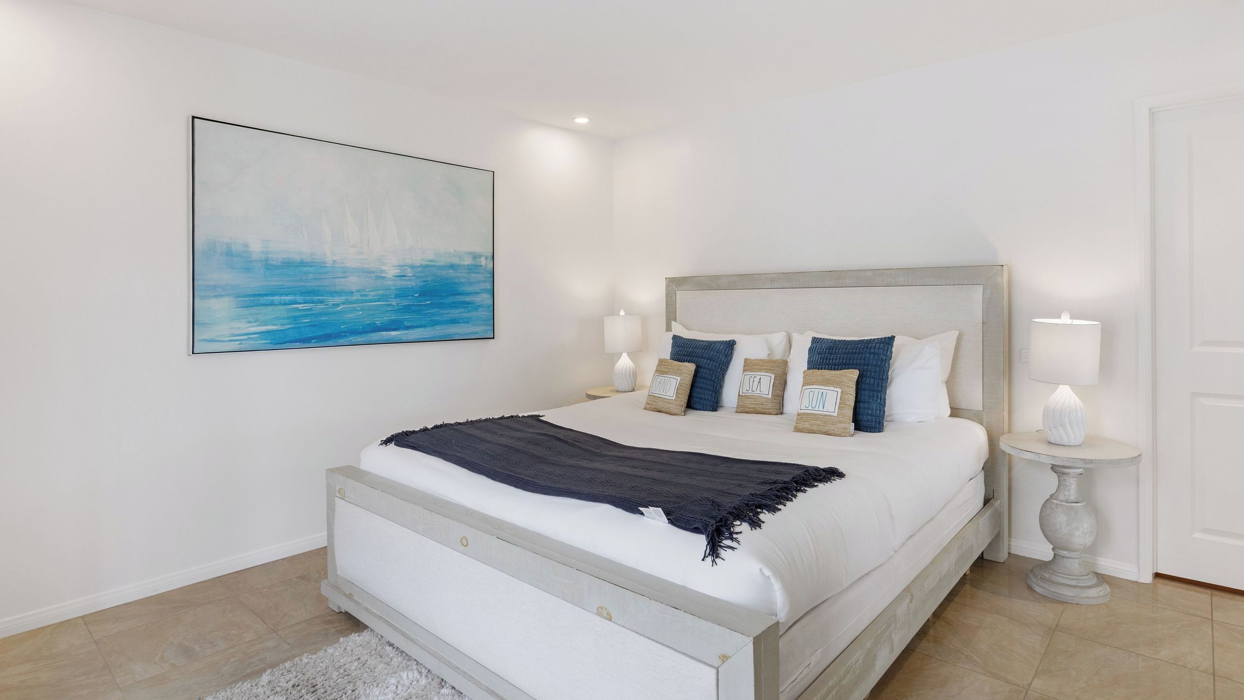 Een slaapkamer met een bed, bedlampen, een nachtkastje, een wanddecoratie en een deur.