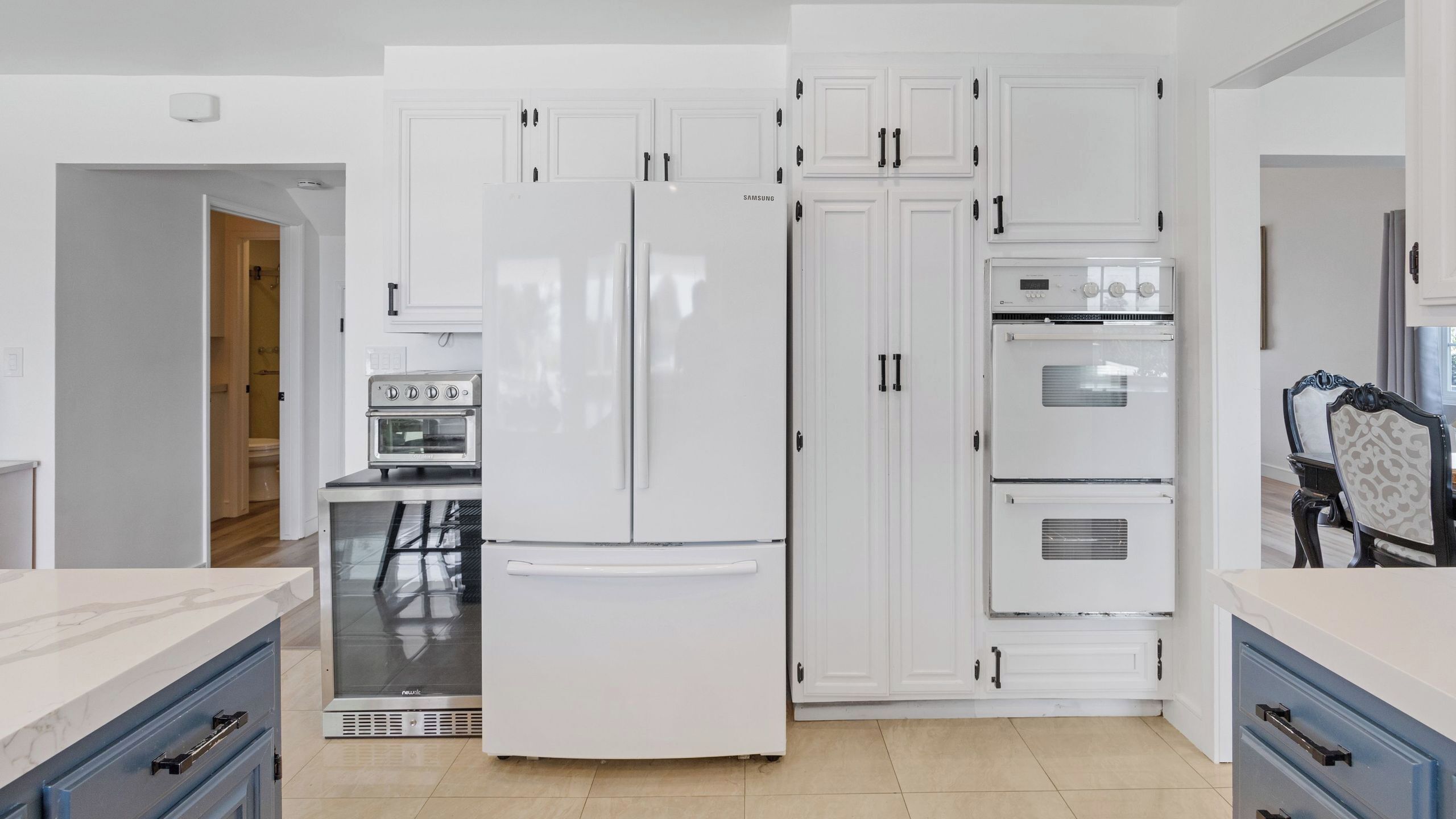 A modern kitchen with white cabinetry, a built-in oven, and a stainless steel refrigerator.