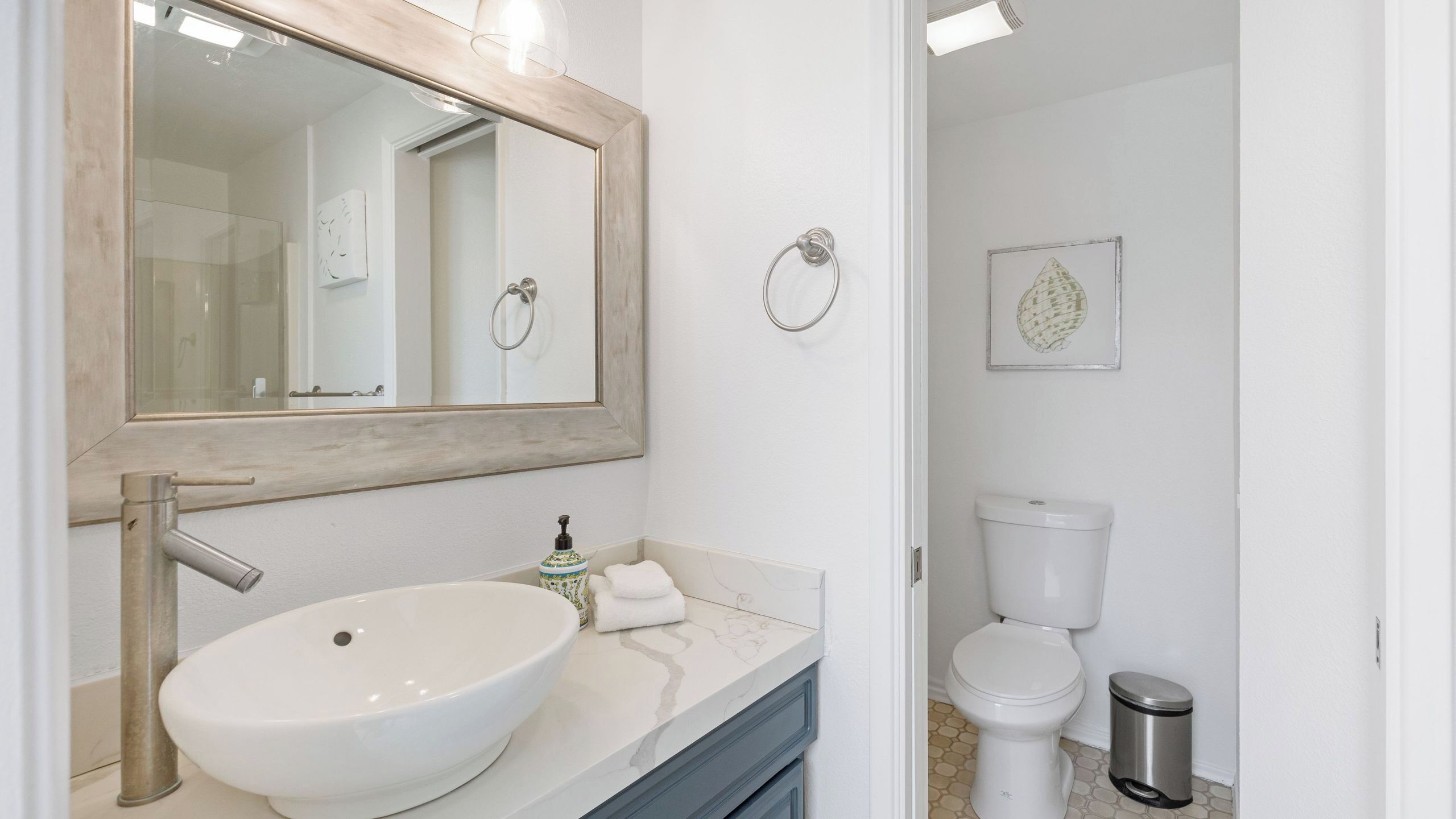 Une salle de bain avec un grand miroir, un lavabo, des toilettes et une poubelle.