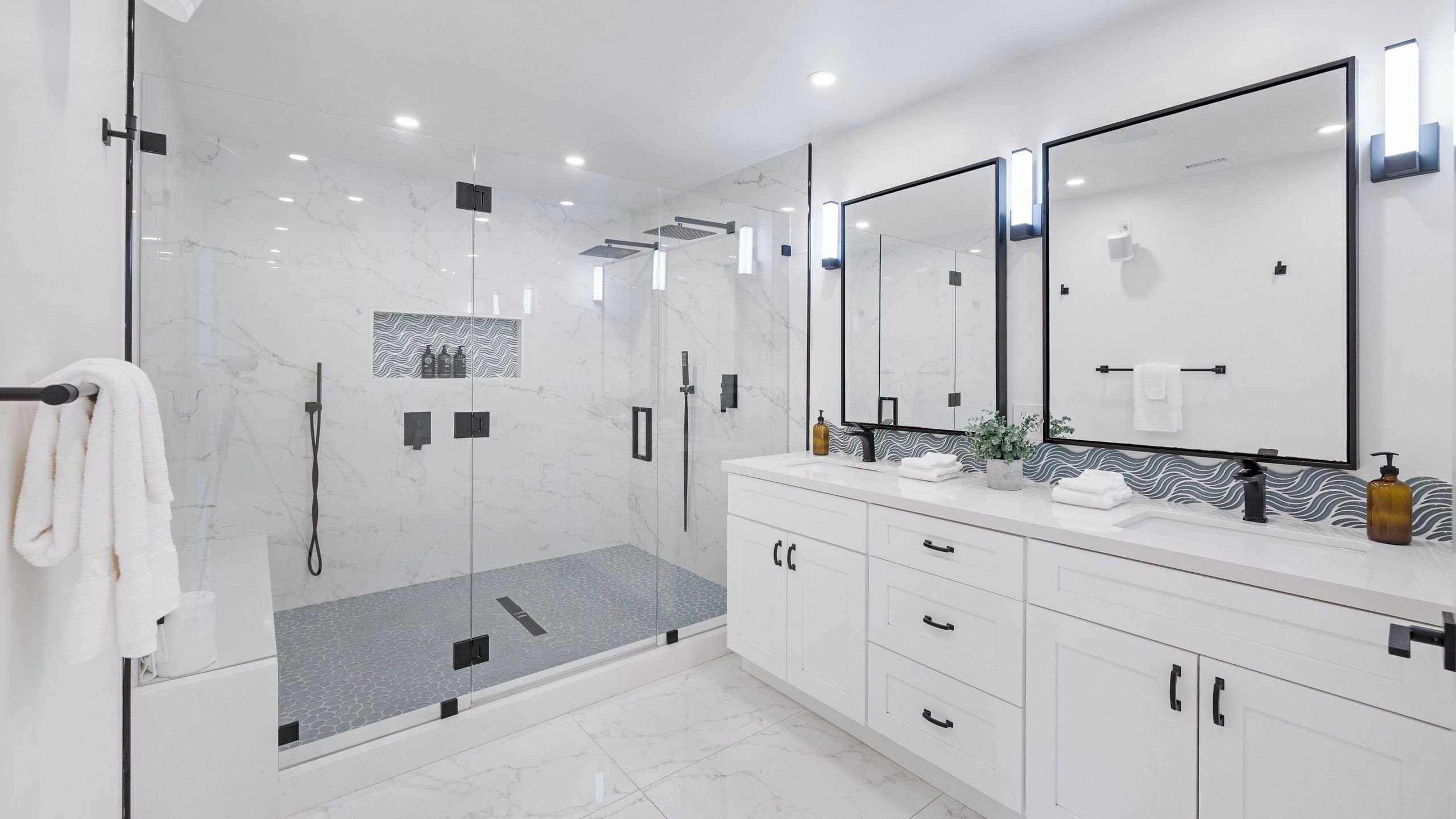 Un baño moderno con ducha envuelta en vidrio, un espejo grande y un tocador blanco con cajones.