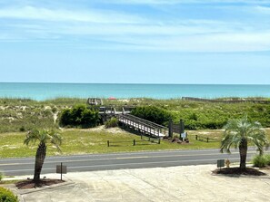 A coastal road with a pedestrian bridge leading to the beach, palm trees, and a clear view of the ocean. - 2BR Holden Beach condo with pool and pet-friendly. (Holden Beach)