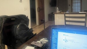 Een kamer met een laptop op een bureau, een stoel, een kapstok, een deur en een raam.