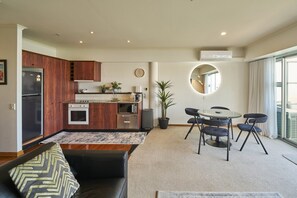 A modern kitchen with wooden cabinets, a dining area with a round table and chairs, and a large window with curtains. - Harbour Views Morning Sun on Iconic Princes Wharf (Auckland City)