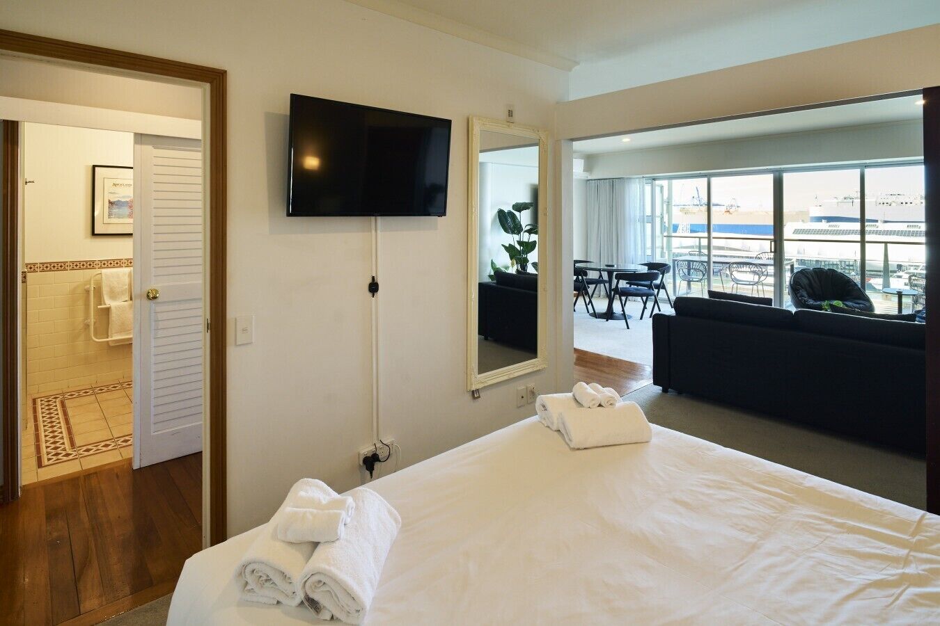Une chambre d’hôtel avec un lit, un téléviseur fixé au mur, une salle de bain avec douche et une vue sur l’extérieur grâce à de grandes fenêtres.