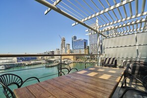 A rooftop terrace with a view of a city skyline, including a distinctive tower and a marina. - Harbour Views Morning Sun on Iconic Princes Wharf (Auckland City)