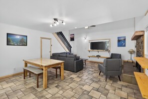 Ein modernes Wohnzimmer mit Esstisch, Sofas, Fernseher und Kamin.