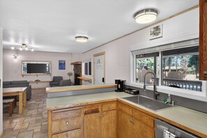 Eine moderne Küche mit integrierter Kaffeestation, einem Essbereich mit Sofa und Tisch sowie einem Ausblick durch ein großes Fenster.