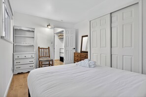 Ein Schlafzimmer mit einem Bett, einem Holzstuhl, einem Schminktisch, einem Spiegel und einem Kleiderschrank mit weißen Türen.