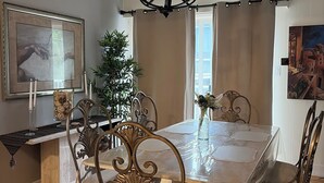 Een eetkamer met een kroonluchter, een lijst met een afbeelding en een potplant.