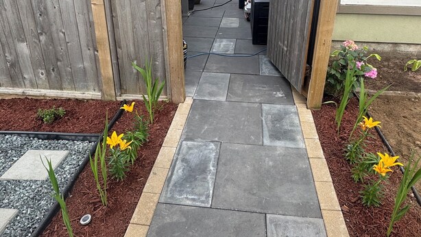Een smal pad dat leidt naar een huis met een houten hek aan beide kanten, omgeven door mulch en planten.