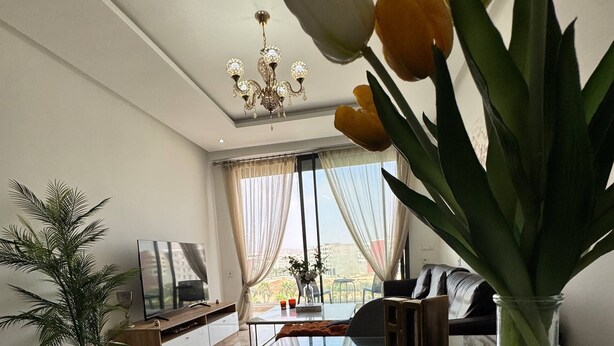 Ein modernes Wohnzimmer mit einem Glastisch, einer Couch, einem Fernseher und einer Kronleuchter.